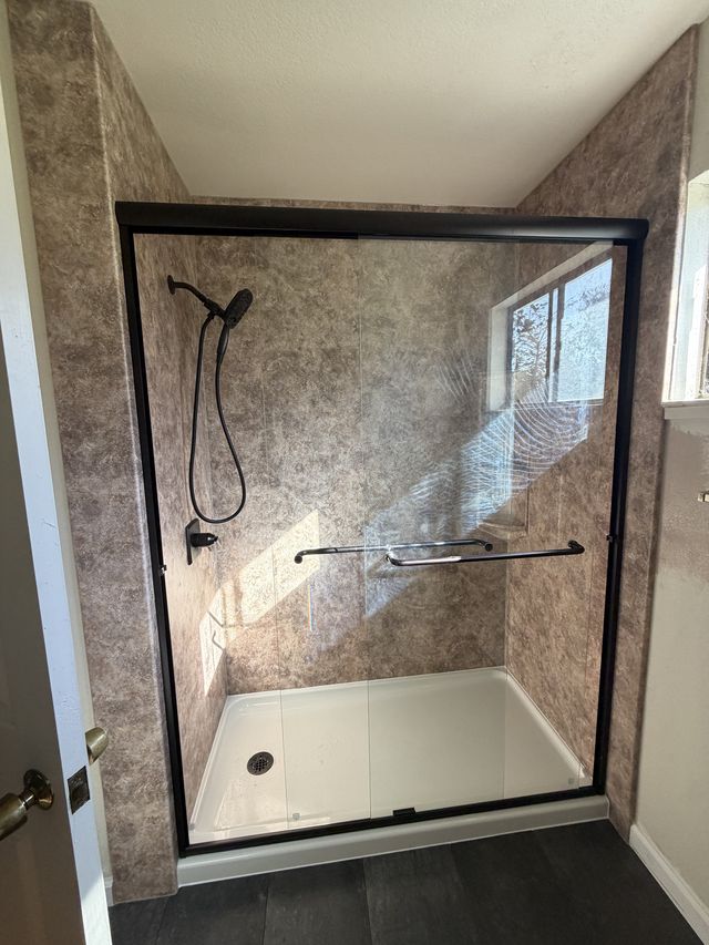Walk-in shower with a black-framed glass door, stone-pattern walls, and a handheld shower.