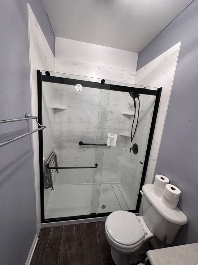 Walk-in shower with black-framed sliding glass doors beside a toilet, with wood-look flooring.