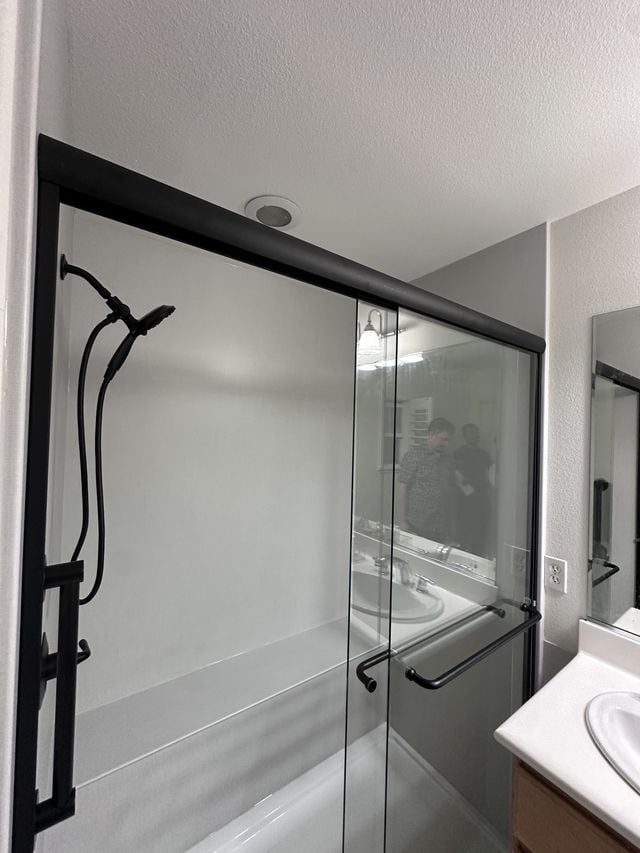 Walk-in shower with black-framed sliding glass doors, a handheld shower, and an adjacent vanity.