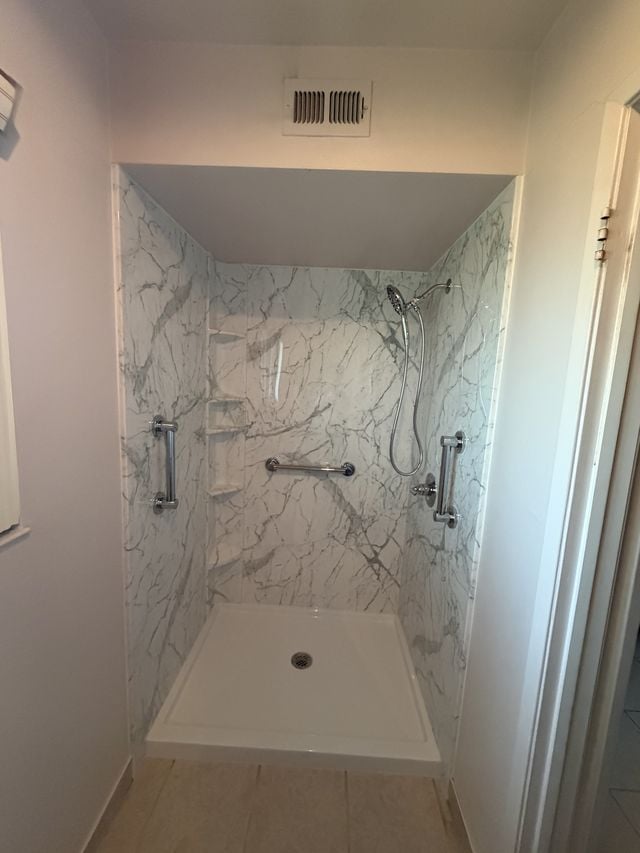 Walk-in shower with white marble-pattern walls, a recessed niche, and a handheld shower.