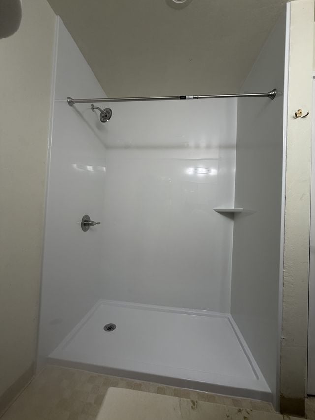 Walk-in shower with smooth white wall panels and a corner shelf.