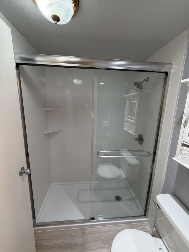 Walk-in shower with sliding glass doors and light wall panels next to a toilet.
