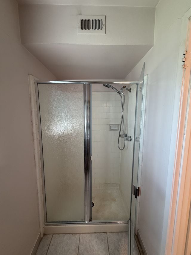 Corner walk-in shower with a framed glass door and marble-pattern flooring.