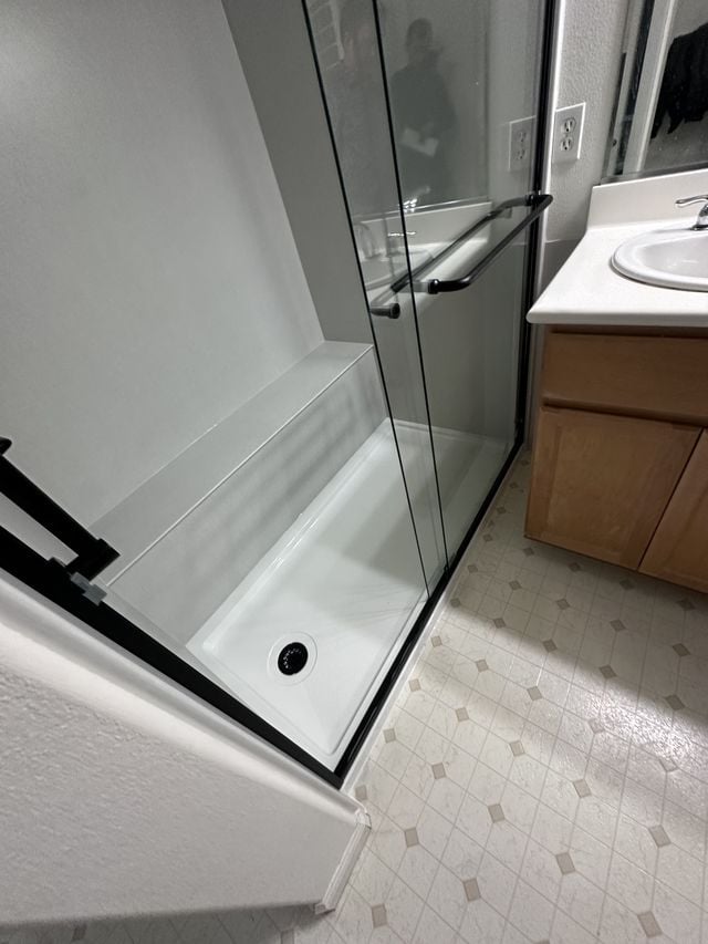 Corner walk-in shower with frameless glass panels beside a wood vanity.