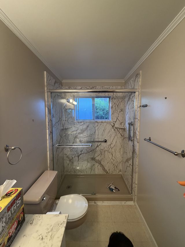 Bathtub and shower with marble-pattern walls, grab bars, a toilet, and a stone-top vanity.