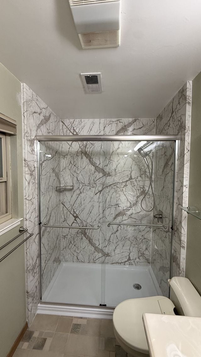 Bathtub and shower with marble-pattern walls, framed glass doors, and a toilet.