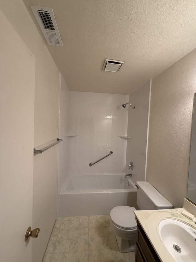 Bathtub and shower with a white surround, a grab bar, a vanity, and a toilet.