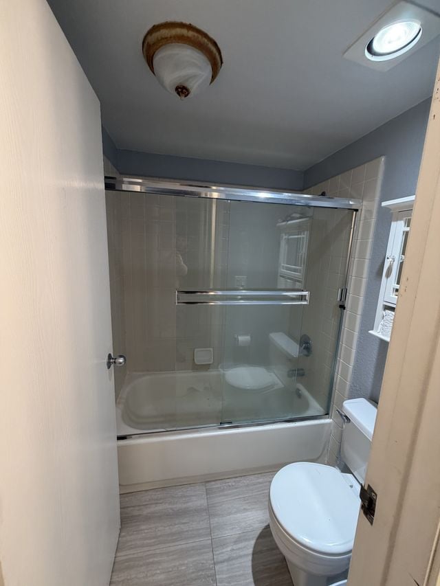 Bathtub and shower combination with framed sliding glass doors beside a toilet.