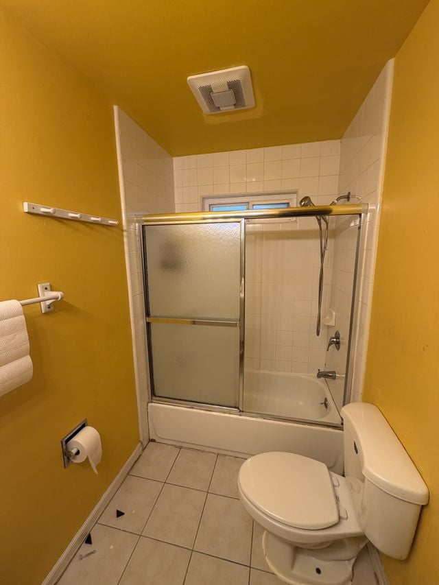 Existing yellow bathroom with a bathtub, framed sliding shower doors, and a toilet before remodeling.