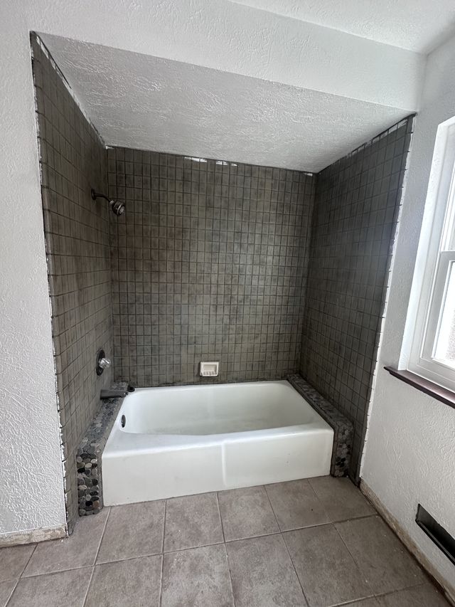 Existing bathtub with a worn dark tiled surround before remodeling.