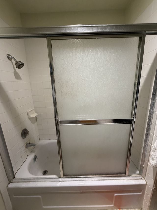 Existing bathtub with framed frosted sliding glass doors and a tiled surround before remodeling.