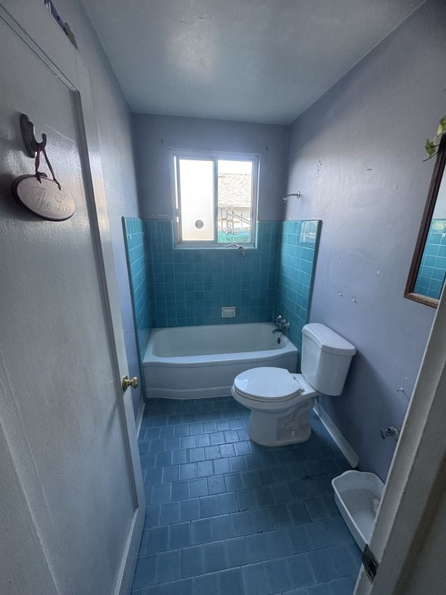 Existing bathroom with a blue-tiled bathtub surround and a toilet before remodeling.
