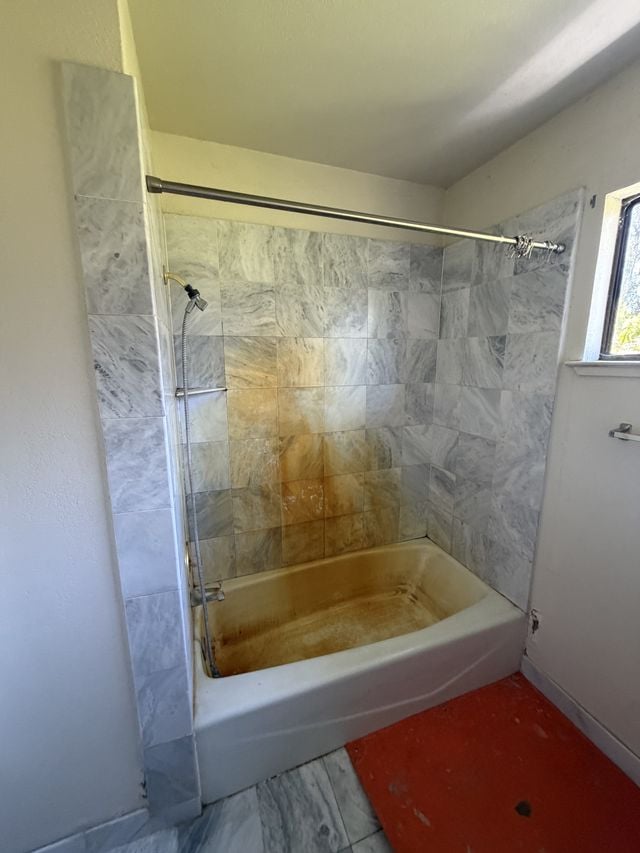 Aging bathtub with staining and marble-pattern wall panels during remodeling.