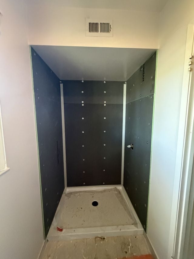 Walk-in shower with dark wall panels and built-in shelf niches during installation.