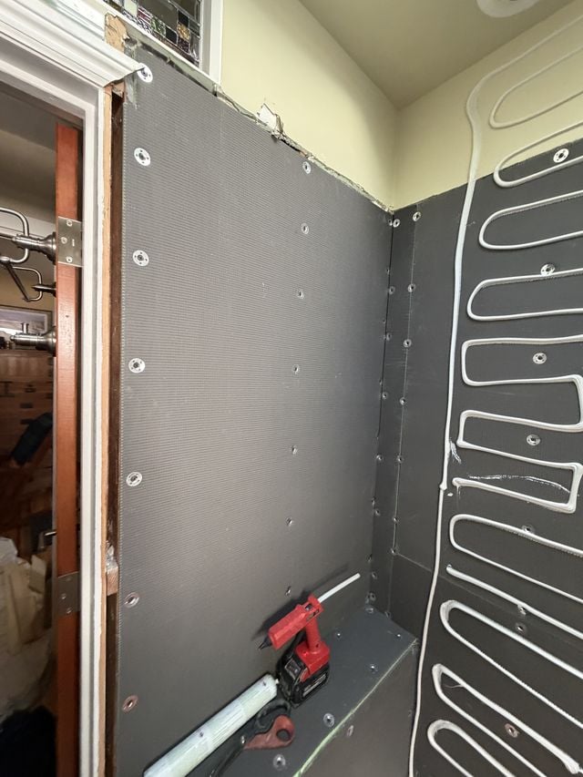 Shower wall preparation with waterproofing membrane, a level, and tools in place.