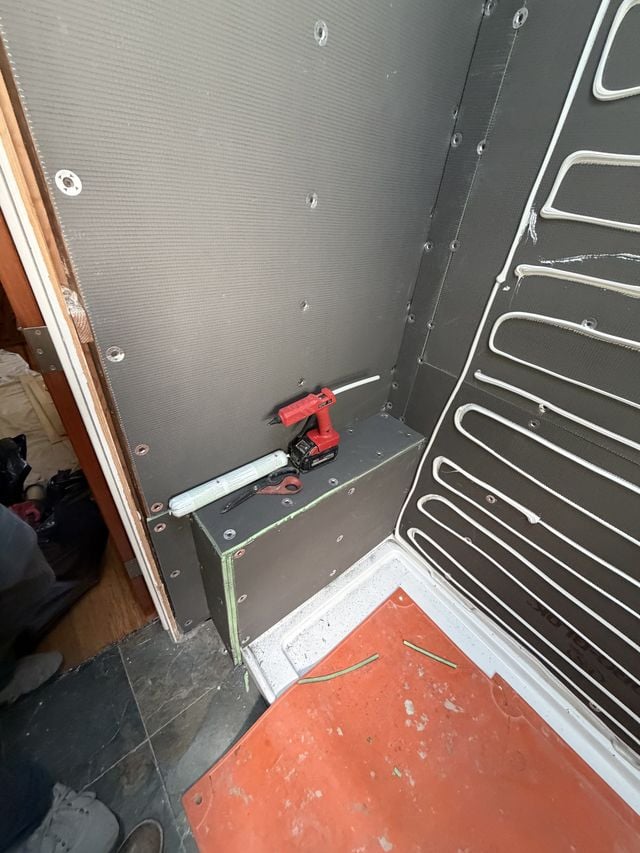 Shower area mid-preparation with waterproofing membrane and floor protection.