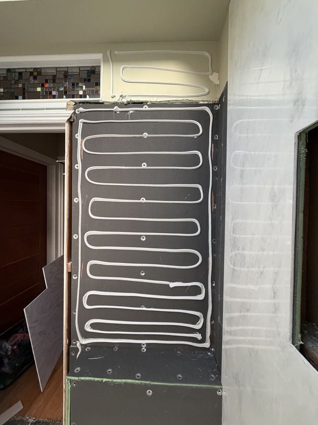 Shower under construction with waterproofing membrane and a tile accent band.