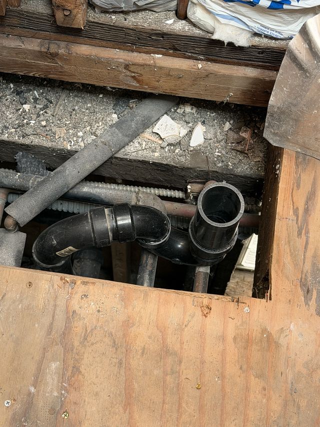 Bathroom subfloor opened during demolition, showing the drain and plumbing pipes.